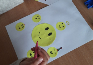 Dzieci wykonują prace plastyczne z żółtych papierowych kółek, na których rysują swoje emocje.